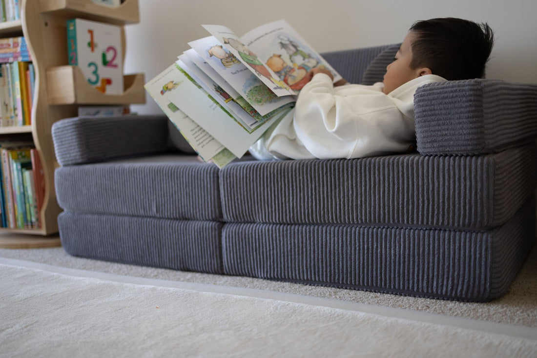 A child relaxing and reading a picture book on a grey corduroy Funsquare play couch in a home playroom